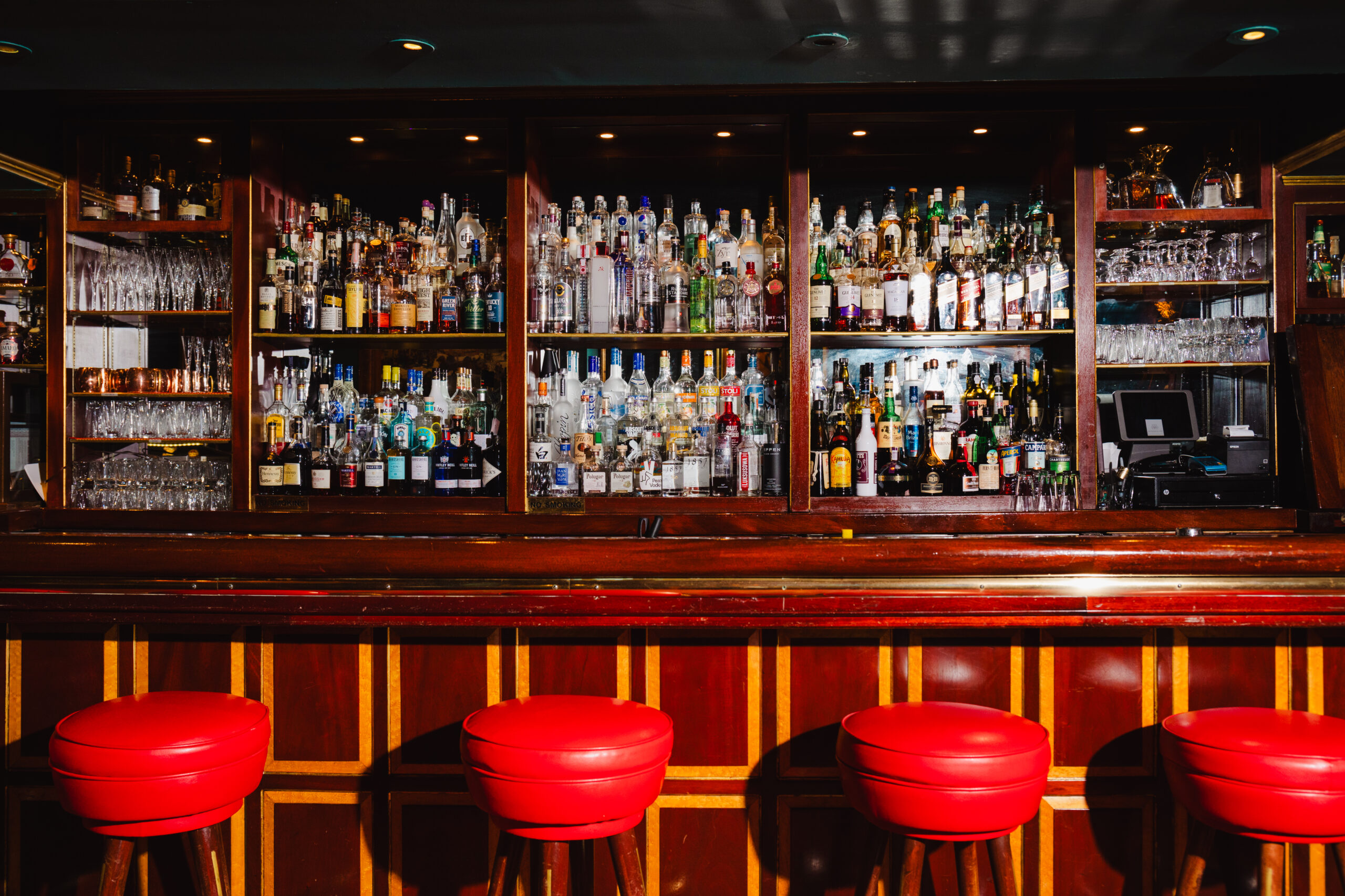 Wooden bar with red stools and shelves filled with various liquor bottles