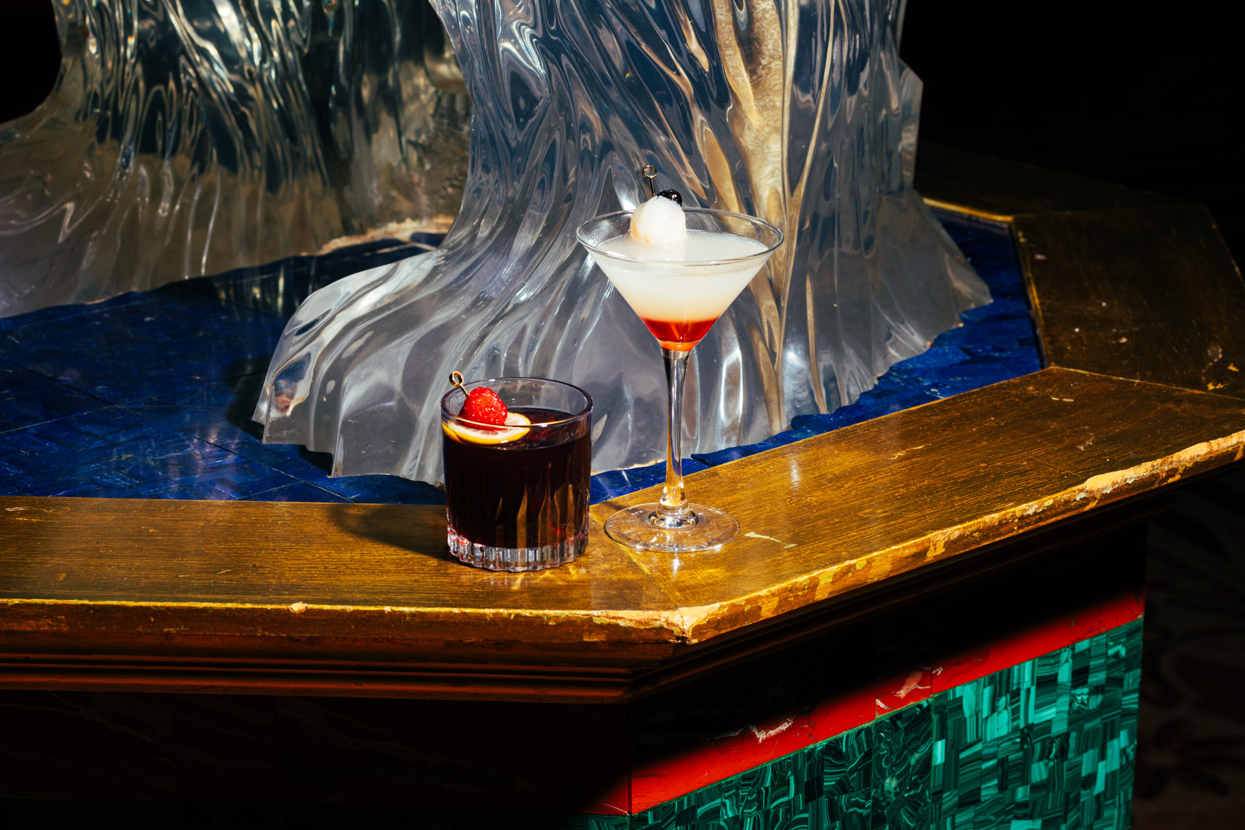 Two cocktails on a wooden table with a blue and clear ice backdrop
