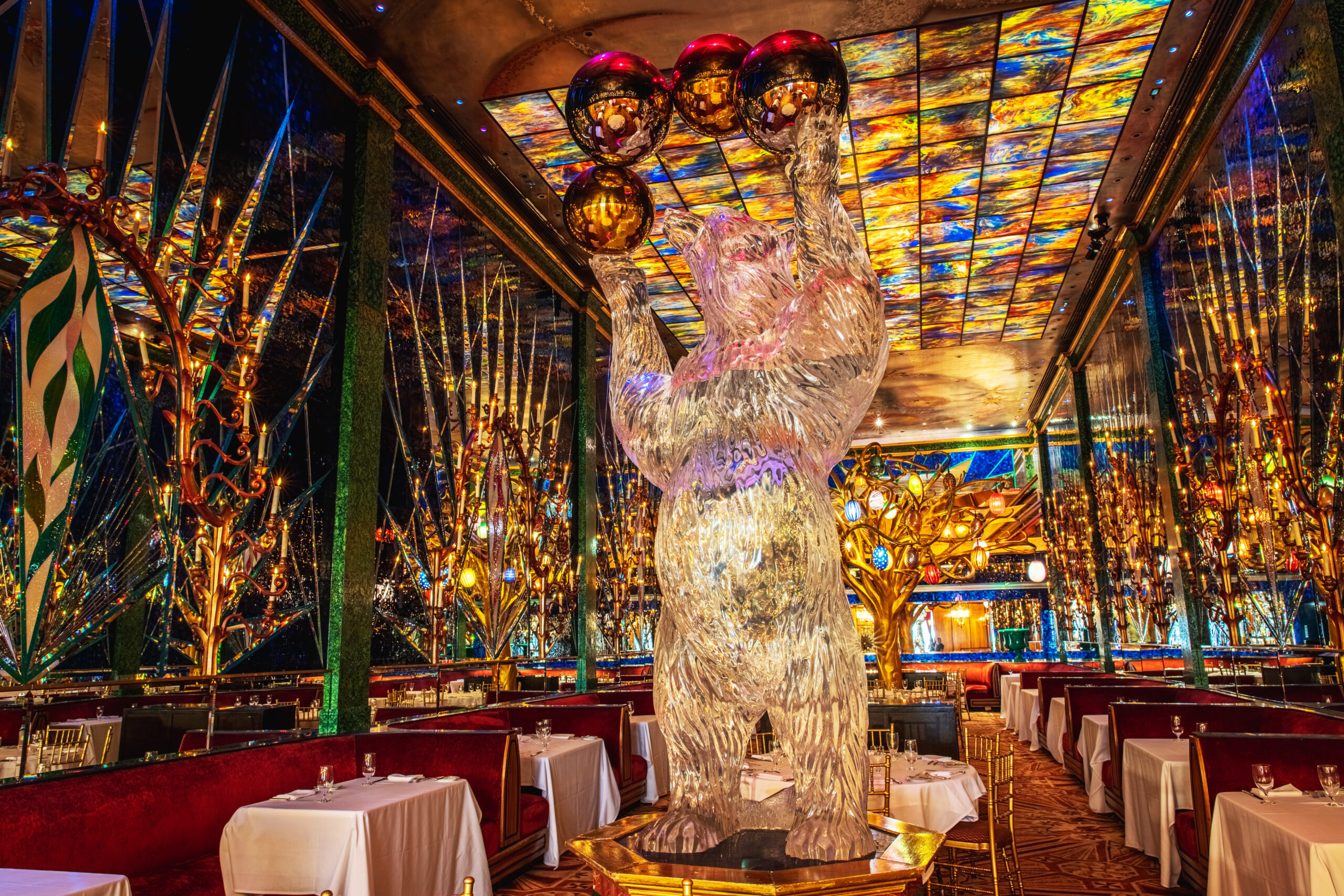 Interior of a restaurant featuring a bear sculpture and colorful stained glass ceiling